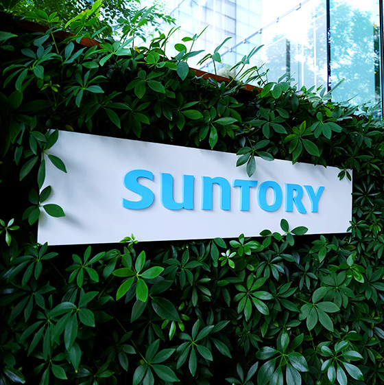 The Suntory logo signage displayed on a wall covered with plants.