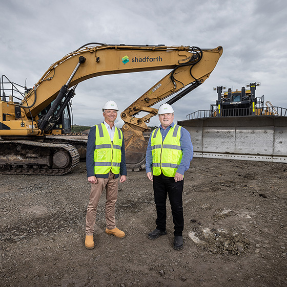 The Suntory Oceania CEO standing in front of an excavator at the Australian Suntory constructions site.