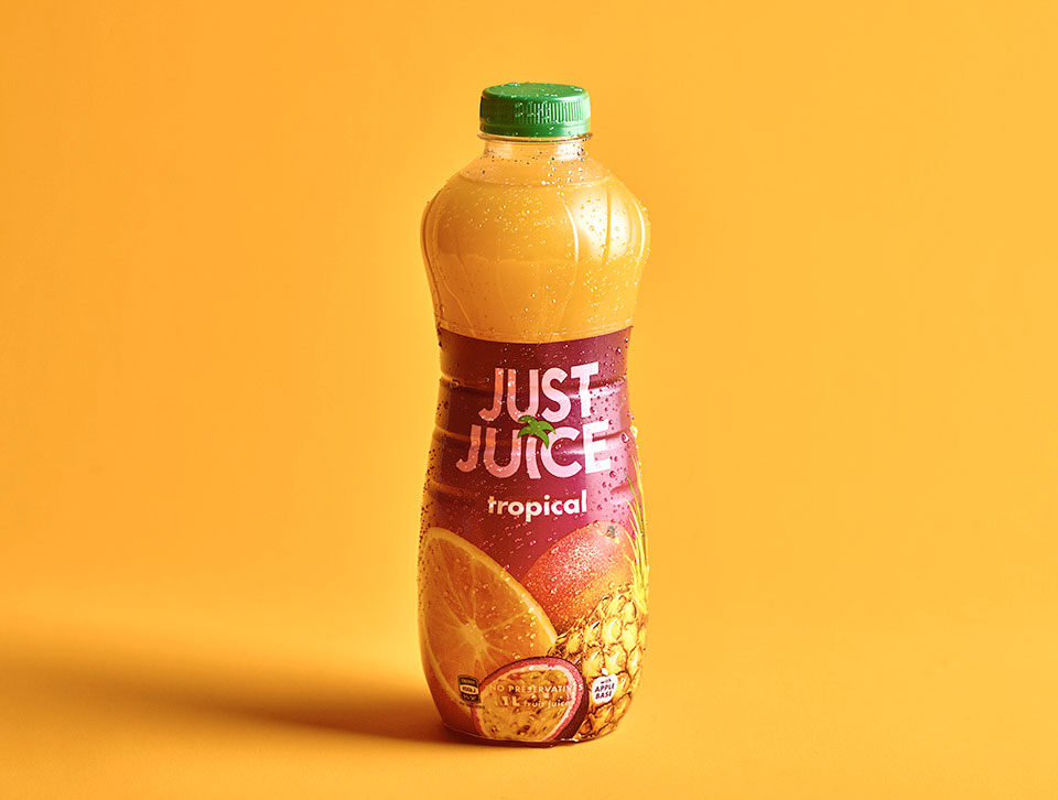 A glass and bottle of Just Juice on an orange background