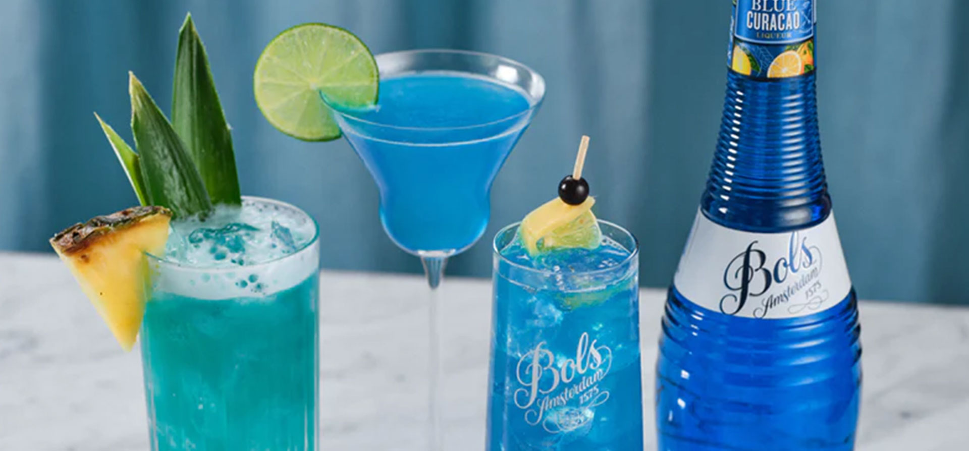 Different types of blue cocktails lined up next to the Bols bottle