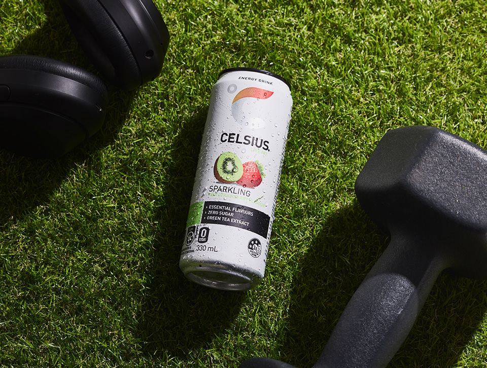 Can of Celsius next to weights on a grass background