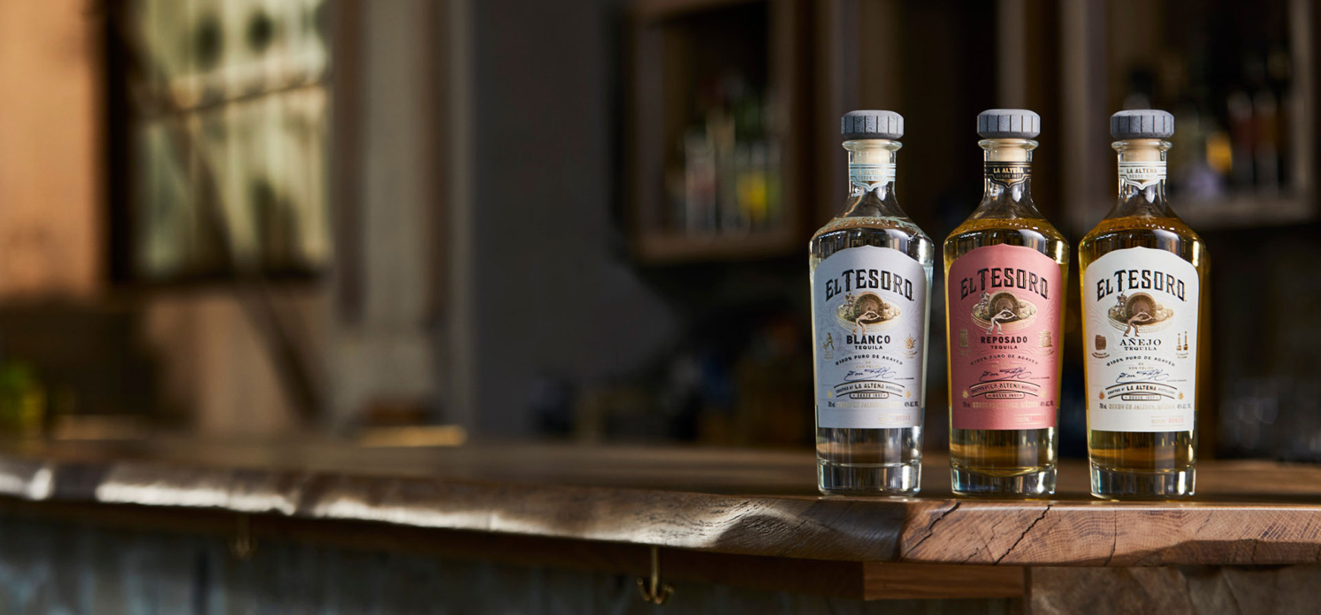 Three bottles of El Tesoro lined up on a wooden bar table