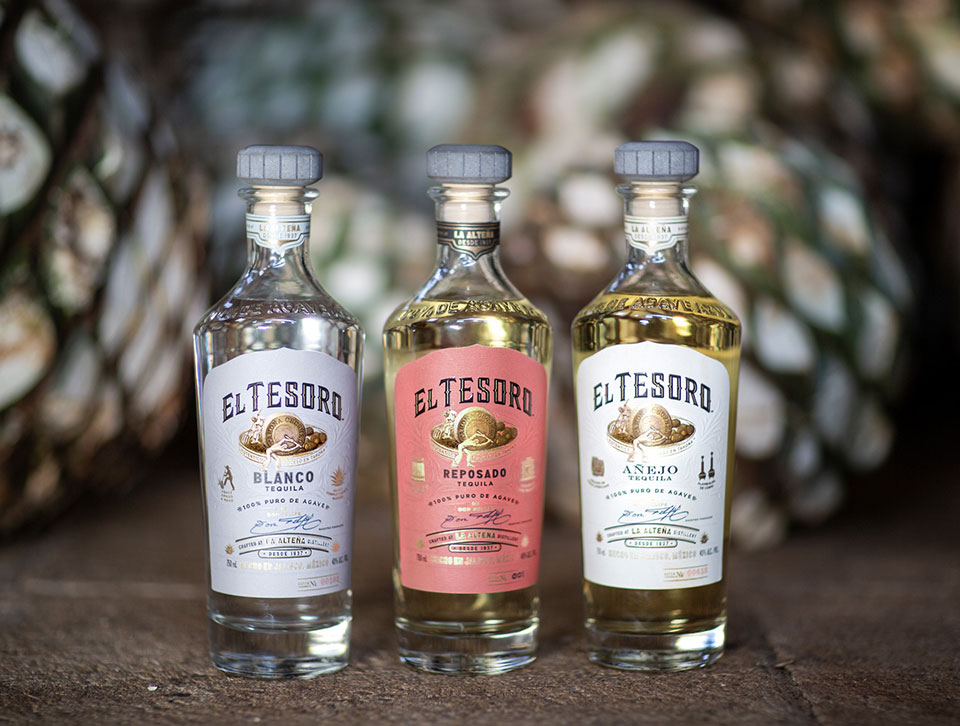 Three bottles of El Tesoro lined with a blurred textured background