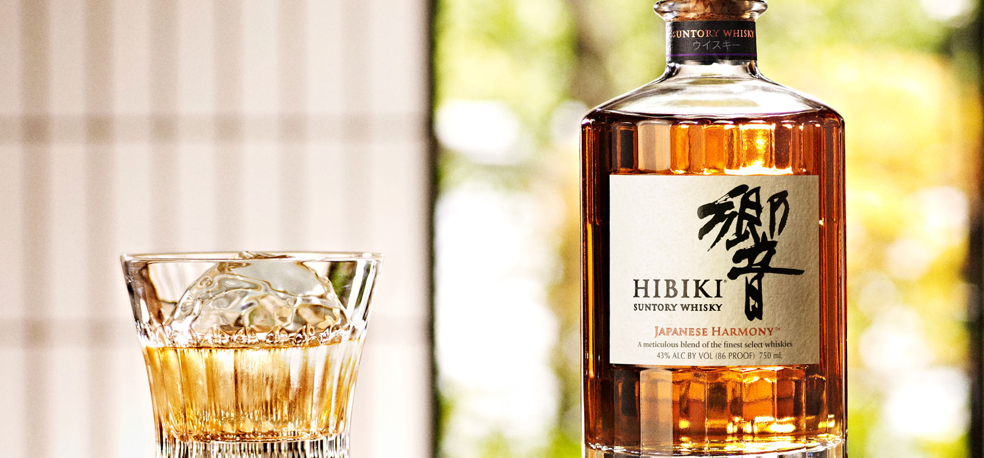 A glass of whisky on the rocks and a Hibiki bottle