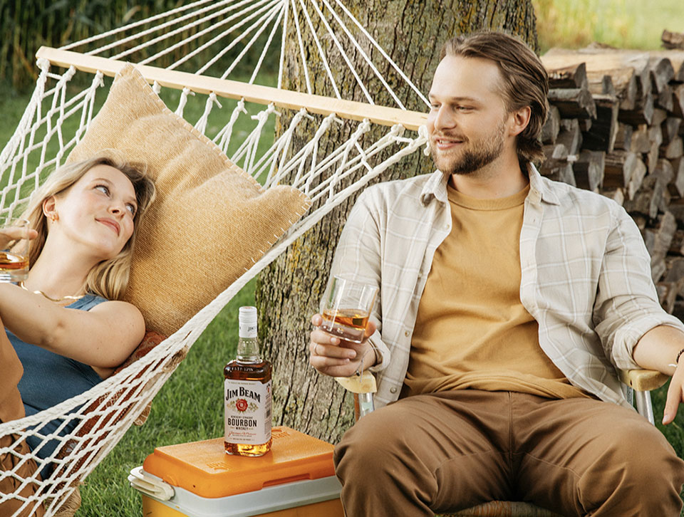 Lady in Hammock and a man sitting down with a glass of Jim Beam