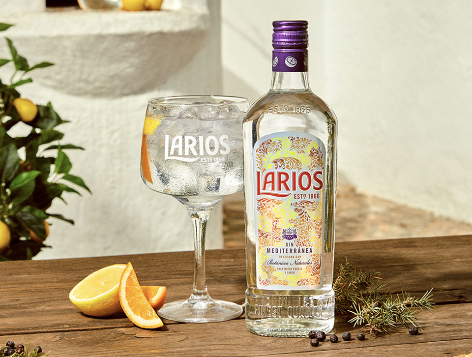 A bottle and glass of Larios gin on a wooden outdoor table 