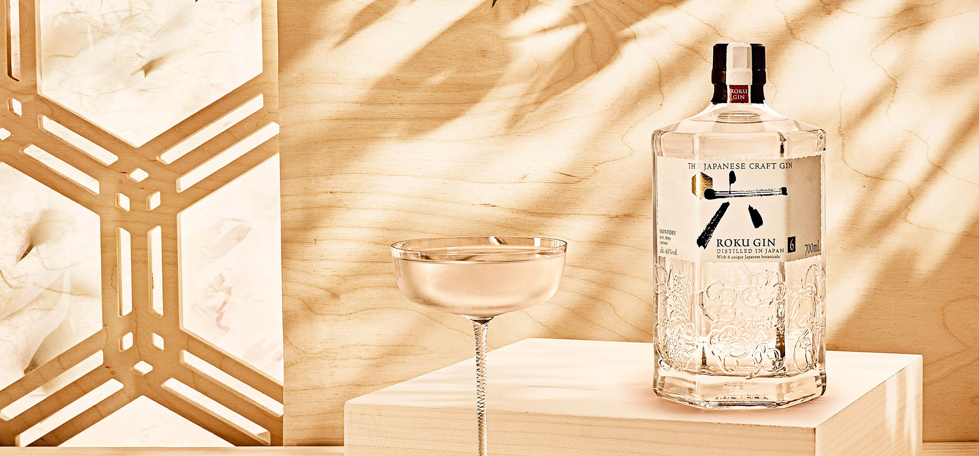 A bottle of Roku and a cocktail glass against a light wooden background