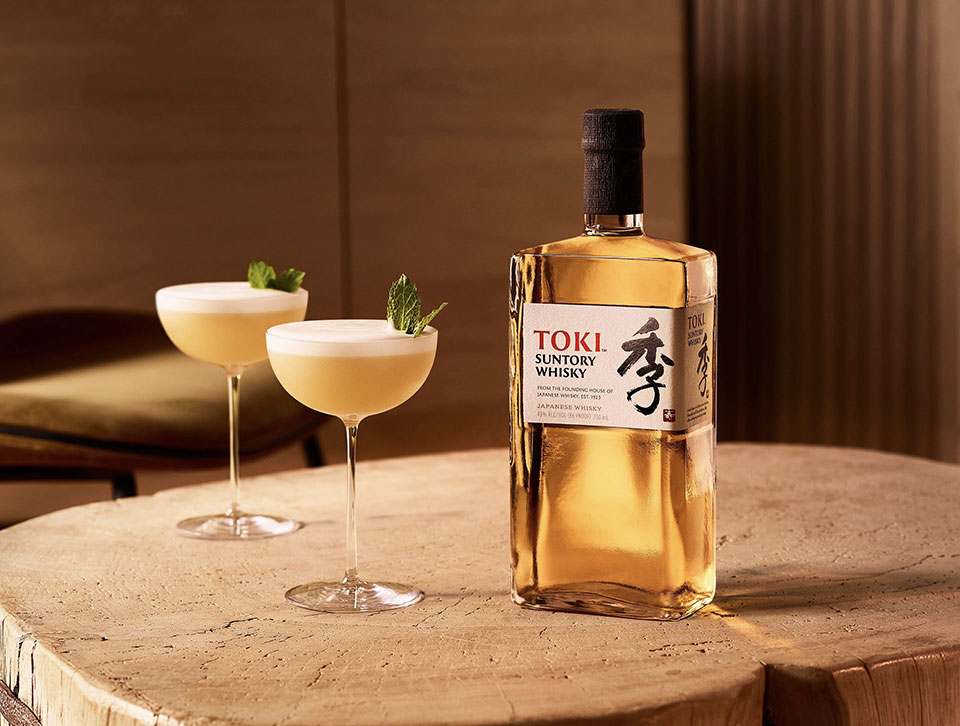 A bottle of Toki and cocktails on a wooden table