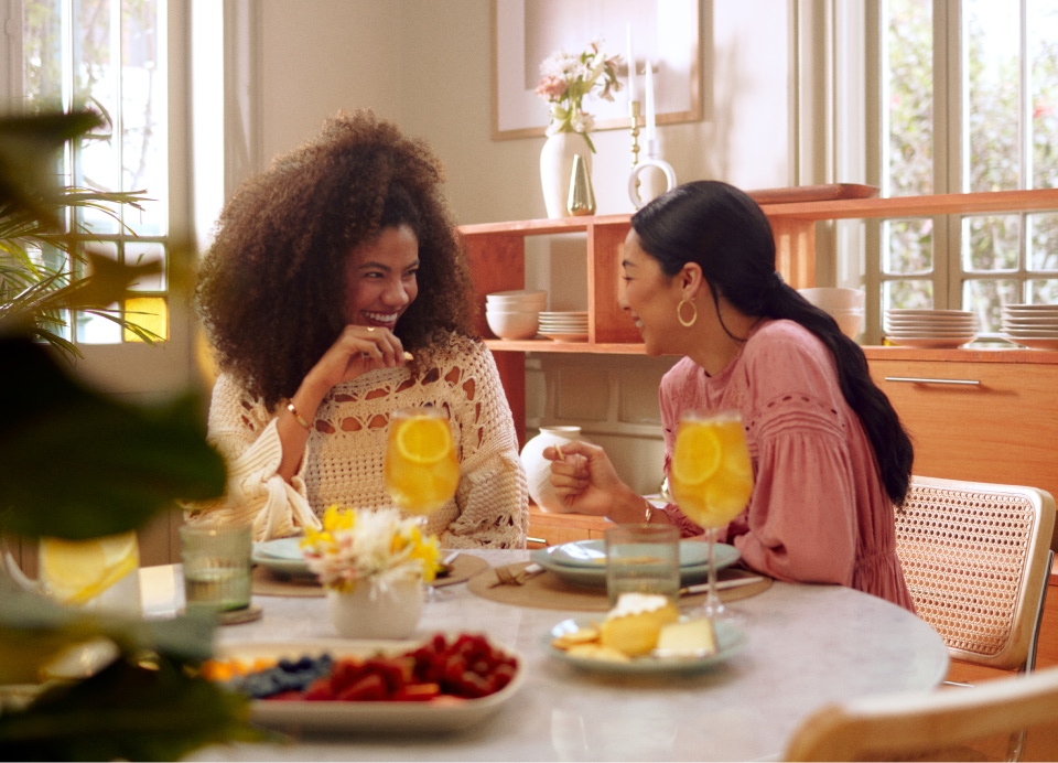 Two ladies sitting at home with fruit, cheese and cocktails