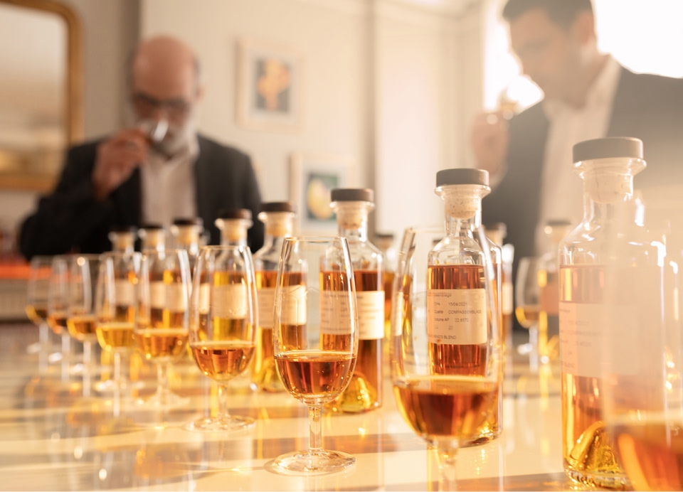 Two men nosing different types of whisky lined up on a table