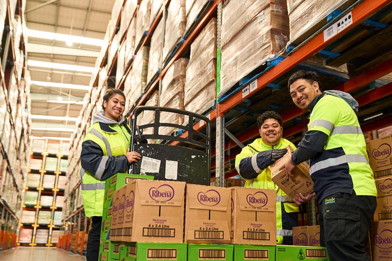 Warehouse workers moving Ribena boxes in a storage area.