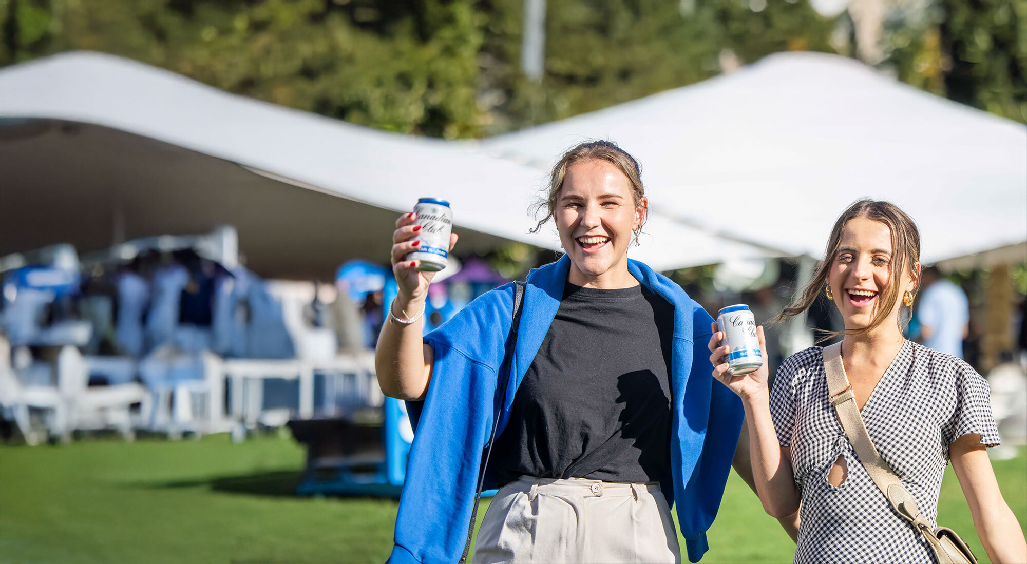 Two people smiling at the camera and drinking Canadian Club RTD outdoors.