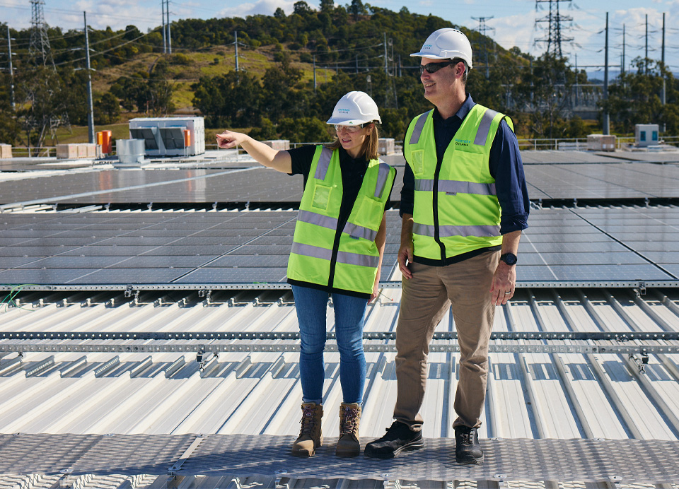 Two workers in high-vis vests standing in front of solar panels