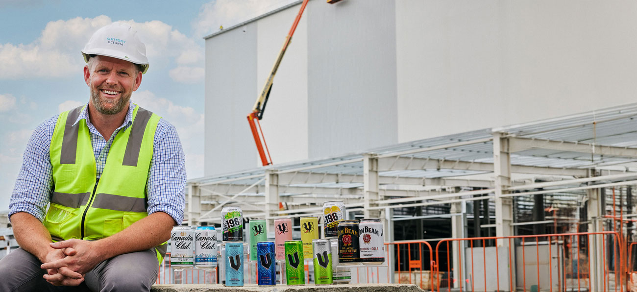 Man in hi-vis and hardhat sitting outside factory next to Suntory Oceania products.