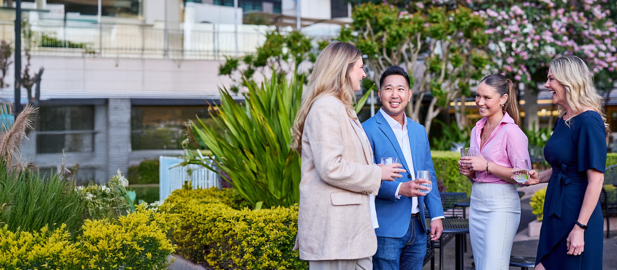 Four office workers talking outside, holding glasses of water