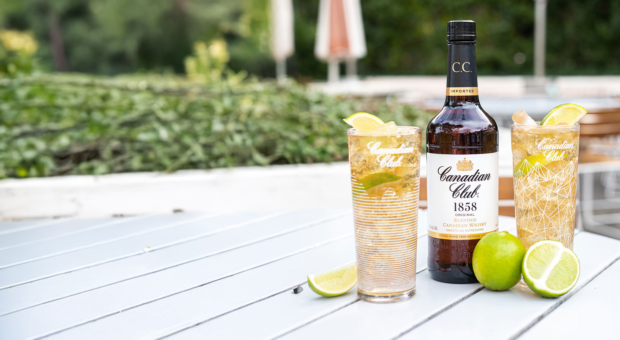 A bottle and glasses of Canadian Club on an outdoor wooden table