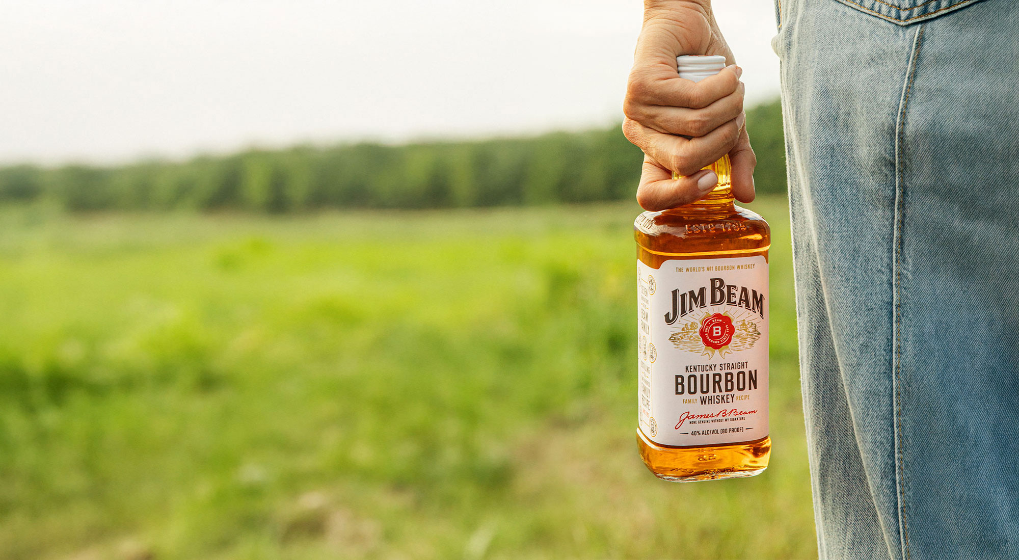 Back shot of a person holding a bottle of Jim Beam in an outdoor field