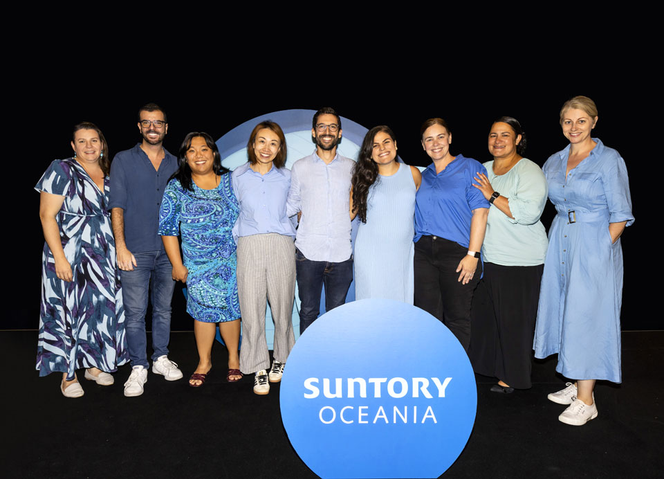 Group of staff standing behind Suntory Oceania logo panel