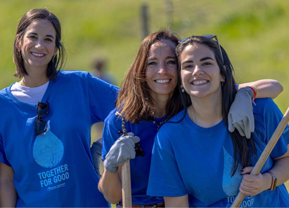 3 people smiling together outdoors wearing a blue shirt labelled "together for good"