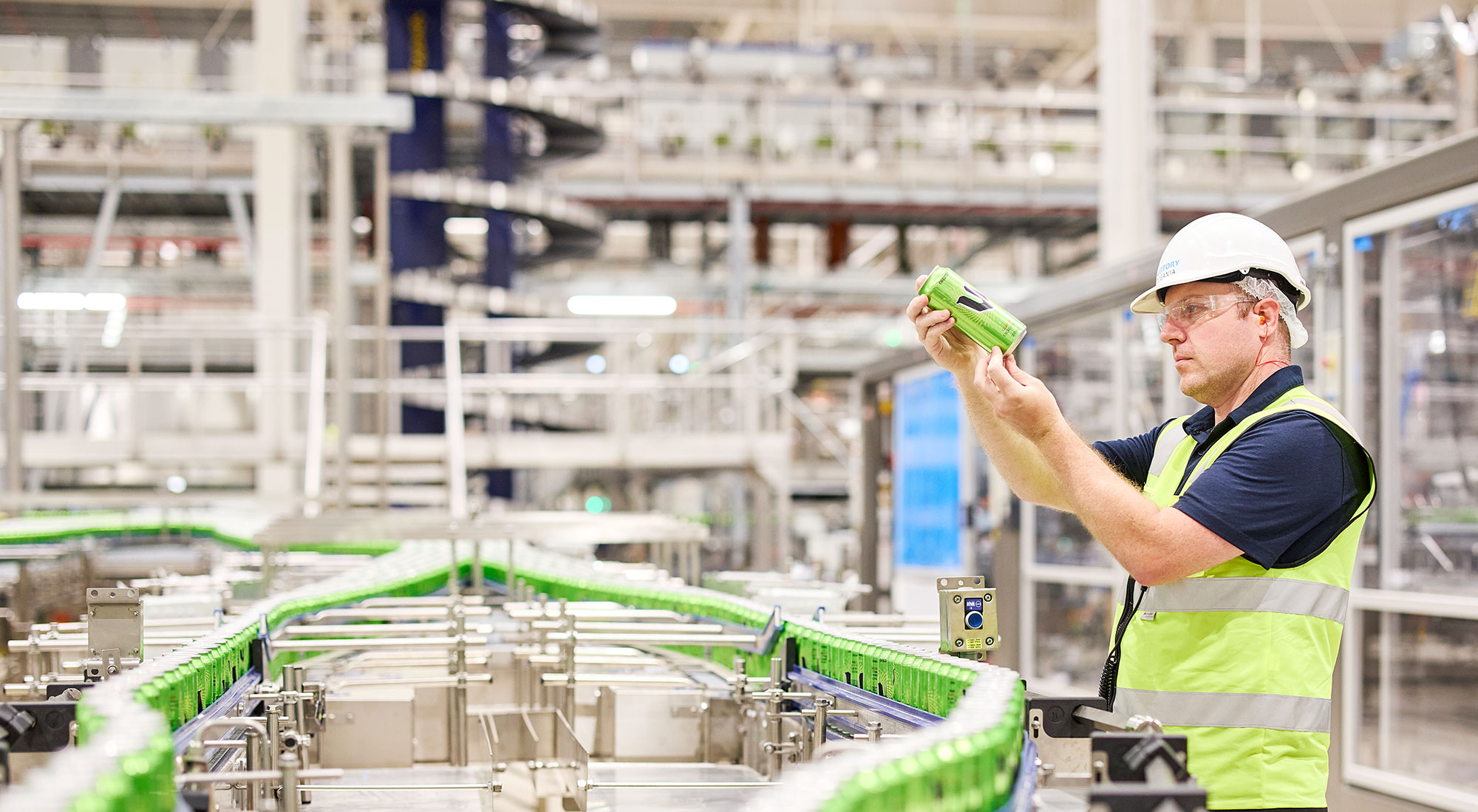 A factory worker inspecting a can of V Energy from the production line